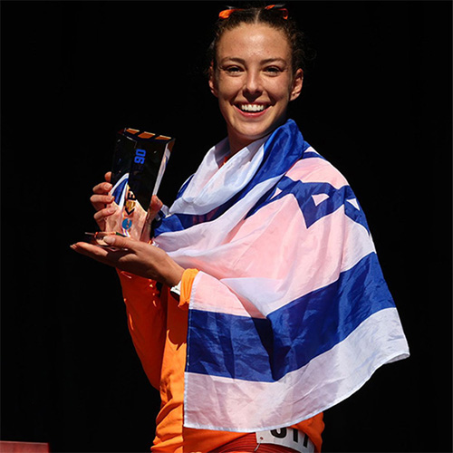 vertical_six.jpg A woman stands holding a trophy from a track competition while an Israel flag is around her shoulders.
