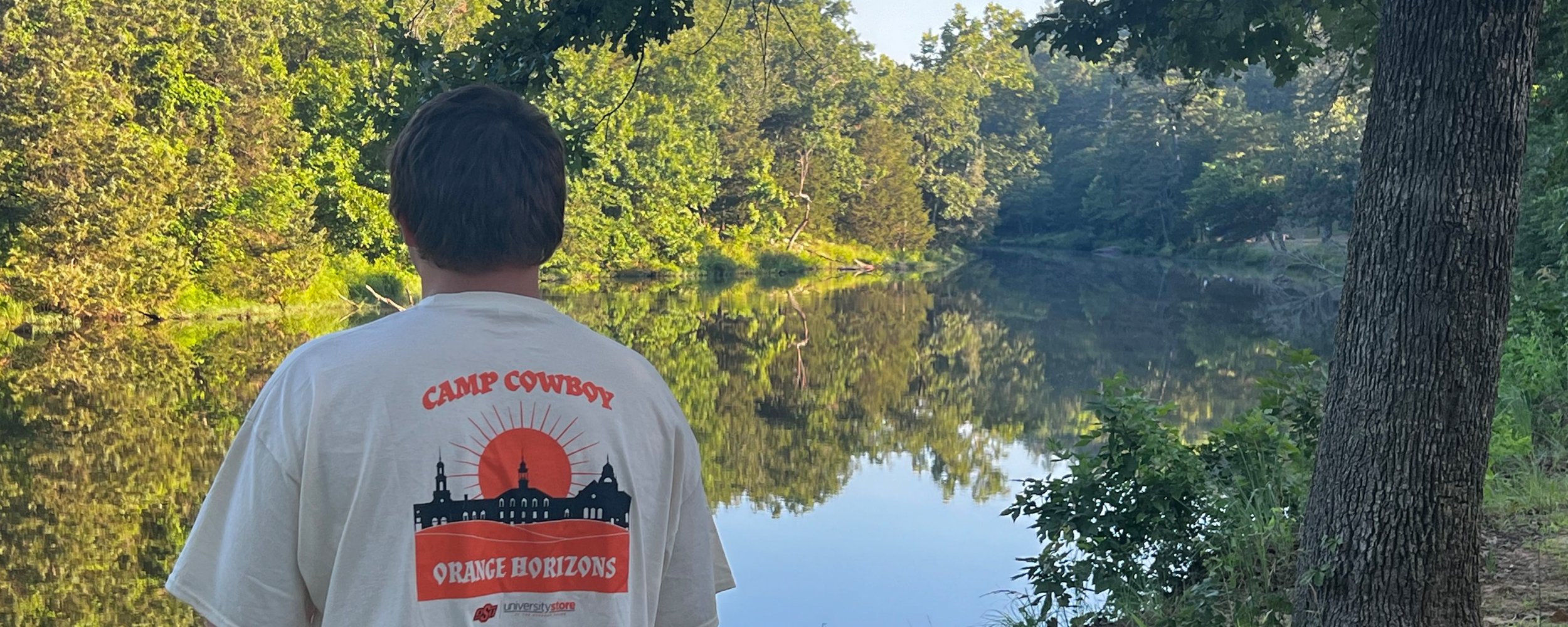 Student overlooks a calm river in a heavily forested area.