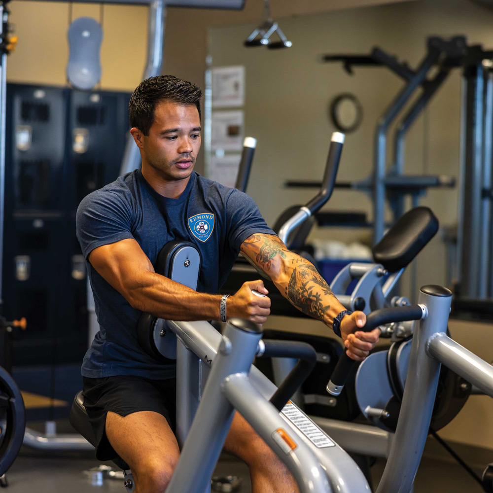 a male police officer wearing workout clothes uses a machine to workout