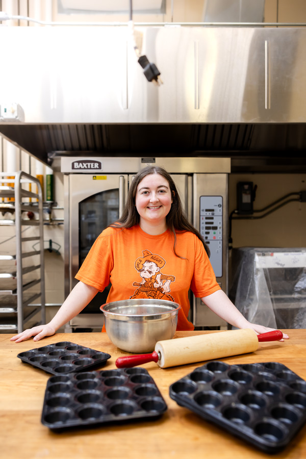 Emily Ward in industrial kitchen with muffin pans, rolling pin and stainless steel bowl scattered along a butcher block countertop