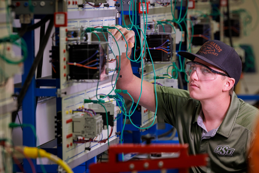 Student adjusts electrical connection on training board in lab.