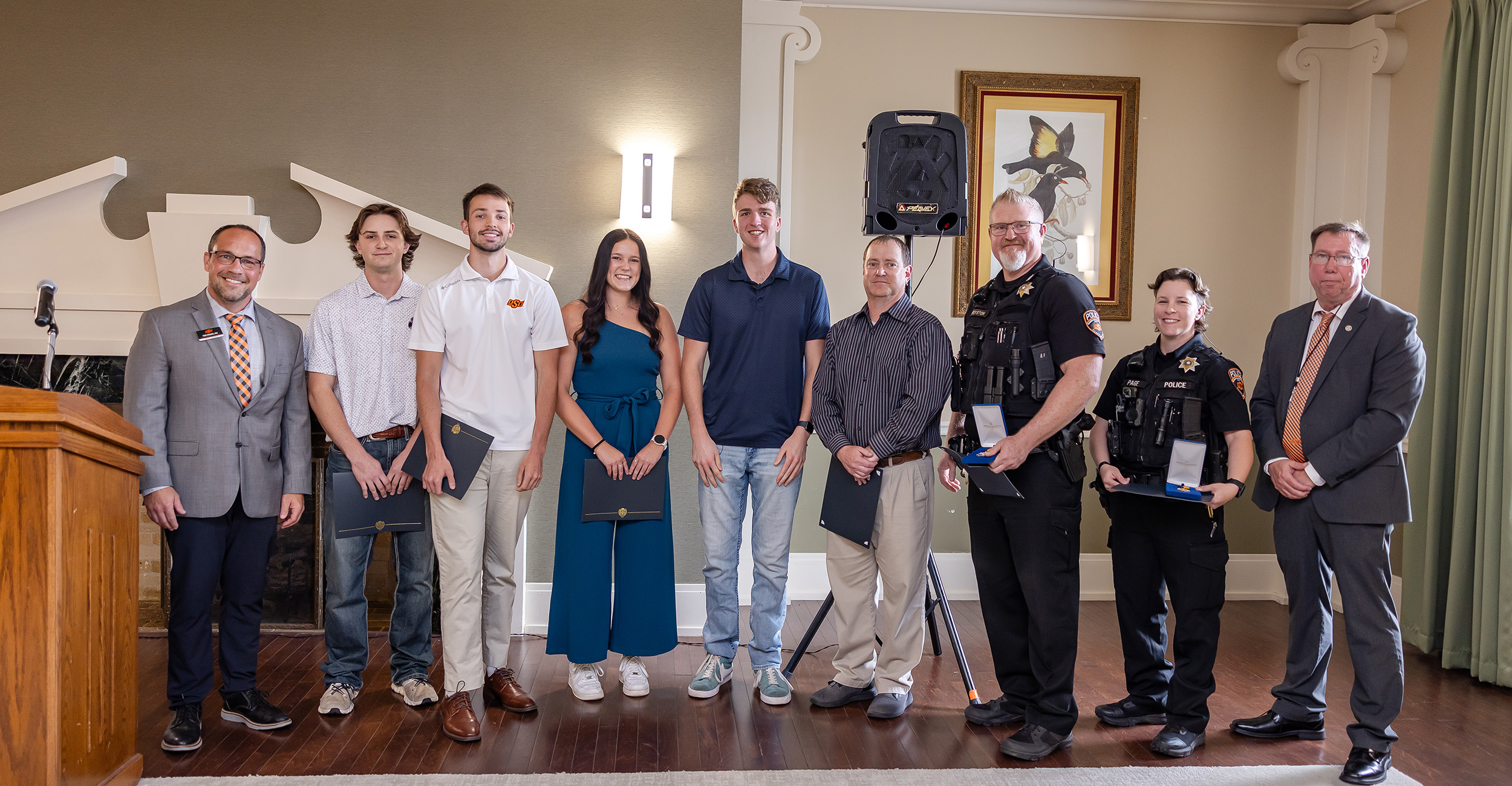 A group of nine individuals, including students, police officers, and university staff, stand in a row indoors during a life-saving award ceremony, smiling and holding certificates or awards. A group of nine individuals, including students, police officers, and university staff, stand in a row indoors during a life-saving award ceremony, smiling and holding certificates or awards.