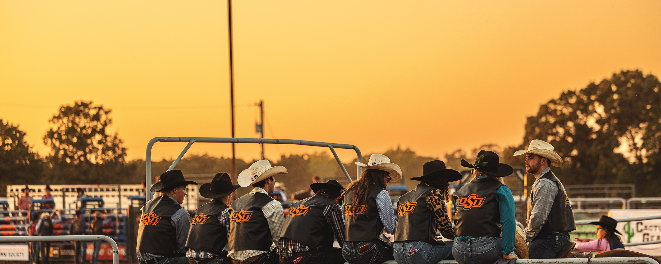A group wearing cowboy hats talk with a yellow sunset in the background. A group wearing cowboy hats talk with a yellow sunset in the background.