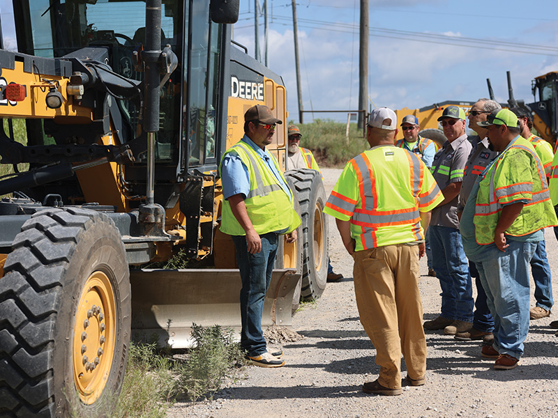 A group of ODOT workers gathered around a Deere Tractor who received motor grader training in Skiatook, Oklahoma, as part of a course through the CTCW.