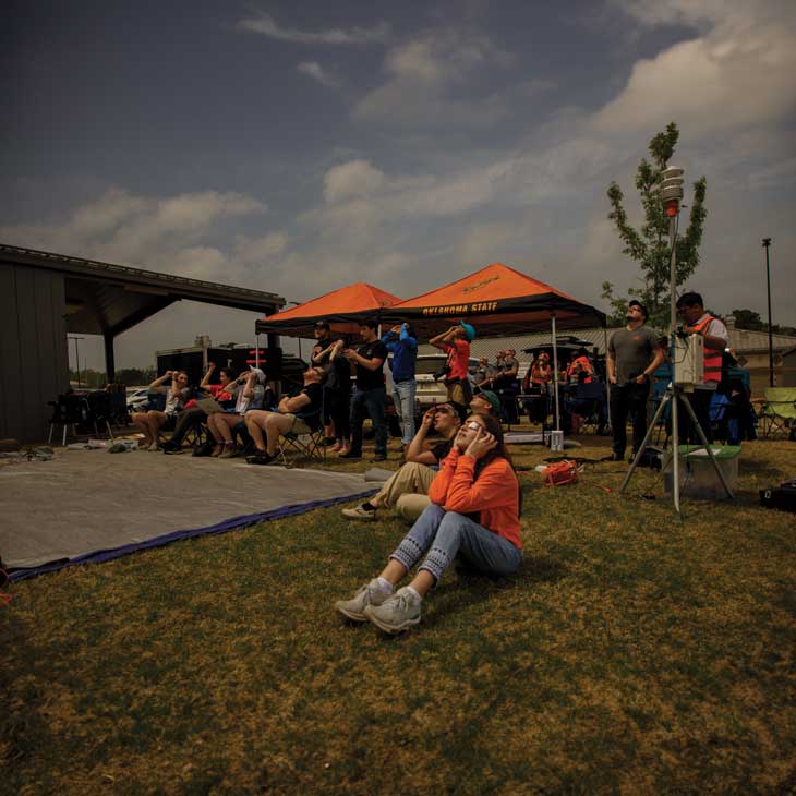 Students sit on grassy hill and watch eclipse